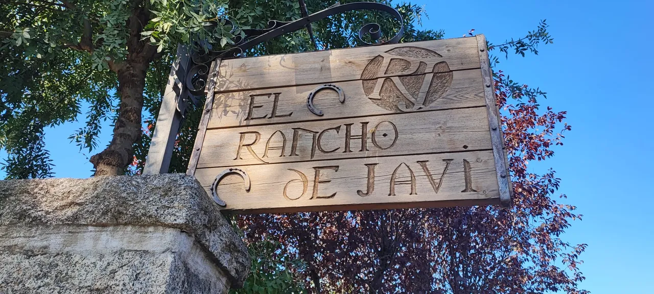 Cartel de madera tallada de El Rancho de Javi sobre el muro de piedra de la entrada principal